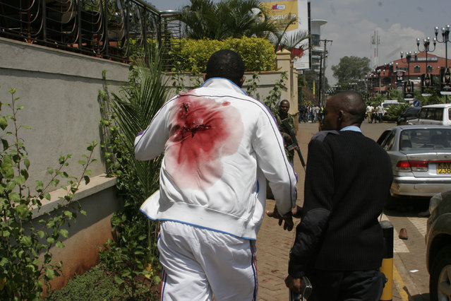 A wounded man is escorted outside the Westgate Mall, an upscale shopping mall in Nairobi, Kenya Saturday September 21 2013, where shooting erupted when armed men attempted to rob a shop, according to police. Witnesses say a half dozen grenades also went off along with volleys of gunfire in and around the mall. (Photo by AP Photo)